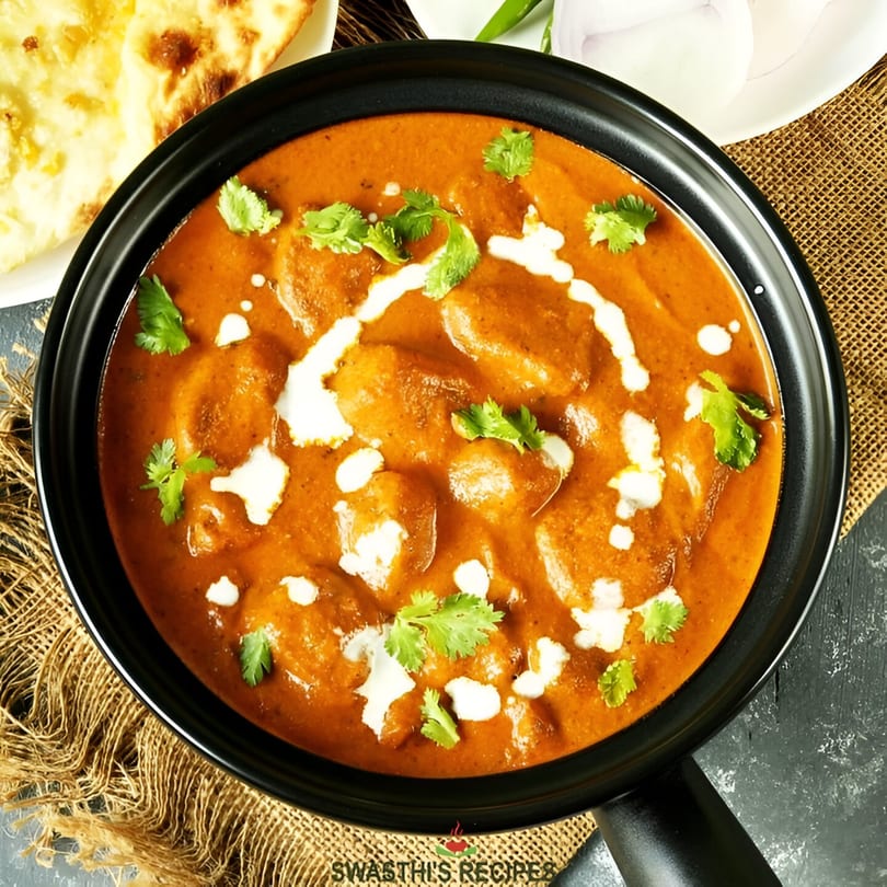 Indian butter chicken or paneer in a black pan, garnished with cream and cilantro, with naan bread.