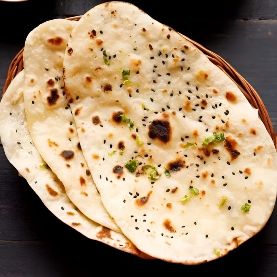 Basket of warm, fluffy Indian naan bread, garnished with black sesame seeds and fresh cilantro.
