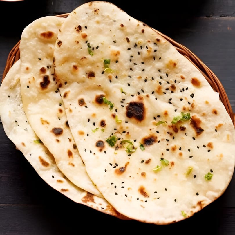 Basket of warm, fluffy Indian naan bread, garnished with black sesame seeds and fresh cilantro.