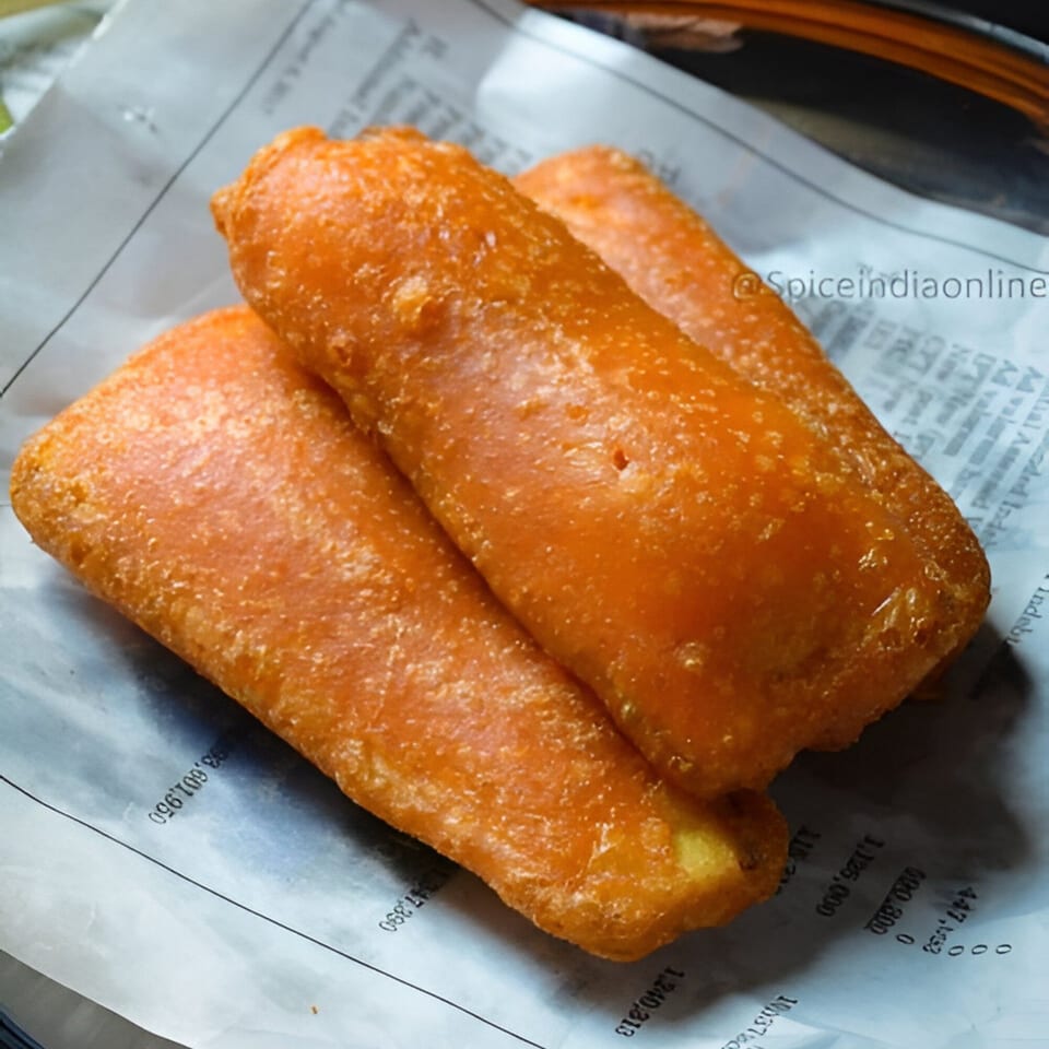 Three golden-brown Indian banana fritters, or Pazham Pori, rest on a piece of newspaper.