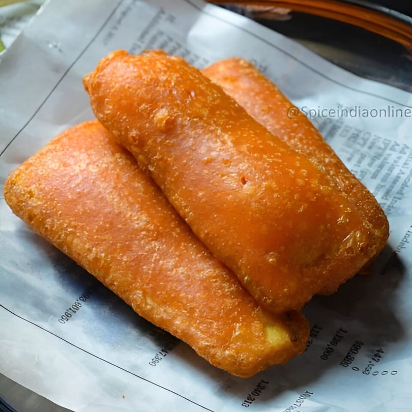 Three golden-brown Indian banana fritters, or Pazham Pori, rest on a piece of newspaper.
