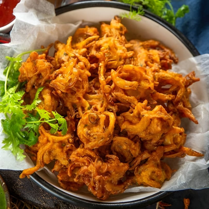 A bowl of crispy, golden-brown Indian onion bhaji, garnished with fresh green cilantro.