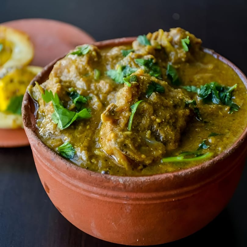 Indian green chicken curry in a rustic terracotta bowl, garnished with fresh cilantro.