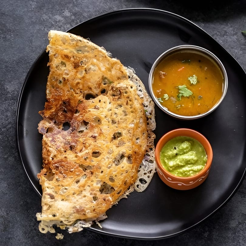 Crispy Indian dosa with a side of green chutney and sambar on a black plate.