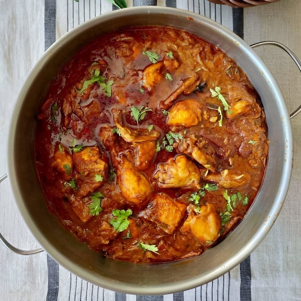 A large metal bowl filled with rich, dark red Indian chicken curry, garnished with fresh cilantro.
